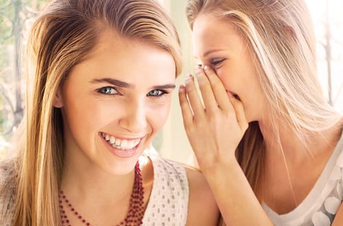 Beautiful smiling as another woman whispering unto her ears